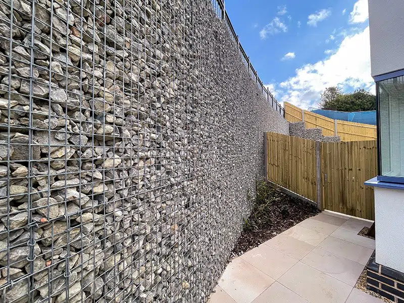 Gabion Retaining Walls by Retaining Walls Tauranga, built with tightly packed stone-filled mesh cages to secure a high boundary beside a modern home.