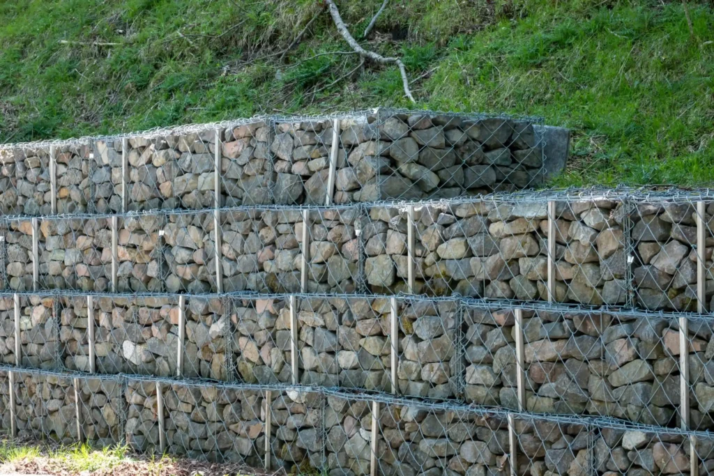 Gabion Retaining Walls by Retaining Walls Tauranga, built with stacked rock-filled wire cages to support a terraced slope on a grassy hillside.