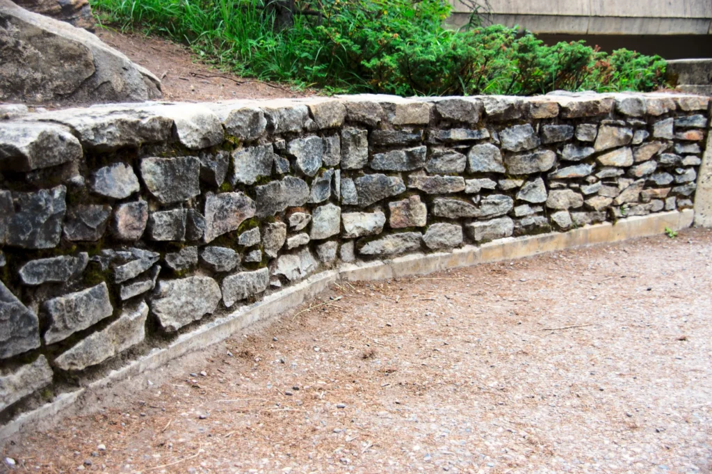 Stone Retaining Walls by Retaining Walls Tauranga, built with irregular natural stones to support a raised garden along a pathway.