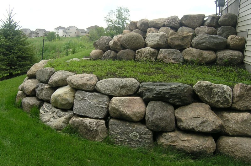 Stone Retaining Walls by Retaining Walls Tauranga, built with large boulders to create a strong and natural-looking tiered landscape near a residential home.