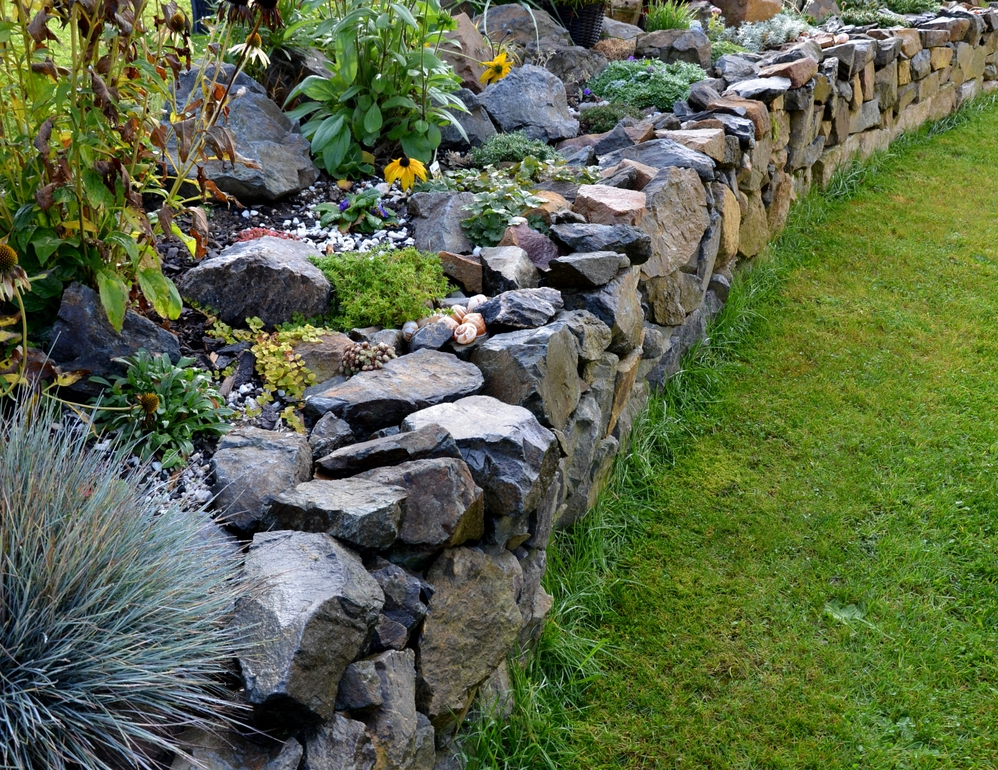 Stone Retaining Walls by Retaining Walls Tauranga, built with rugged rocks to support a raised flower bed in a landscaped garden.