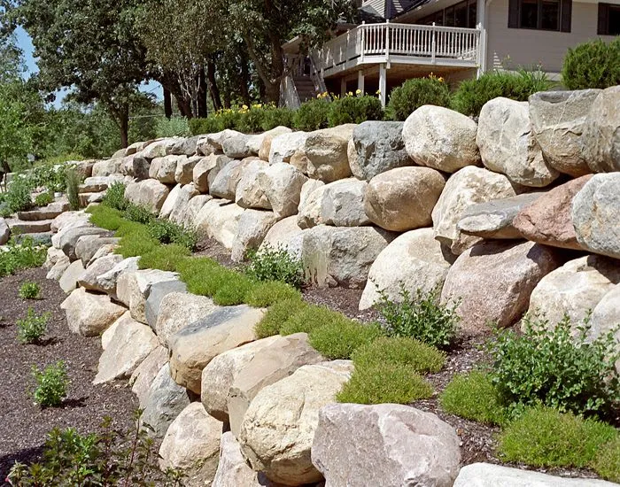 Stone Retaining Walls by Retaining Walls Tauranga, featuring large natural boulders arranged in tiers to support a landscaped slope in a residential yard.