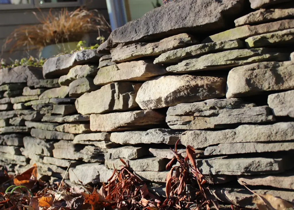 Stone Retaining Walls by Retaining Walls Tauranga, built with flat stacked stones to support a raised garden bed along a residential home.